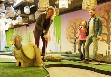 Een gezin met een dochter speelt een potje indoor minigolf in de Market Dome van Center Parcs Park Bostalsee.