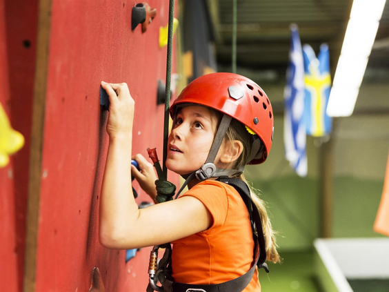 Een meisje met een helm en klimgordel klimt geconcentreerd omhoog op de indoor klimwand in de Adventure Factory.