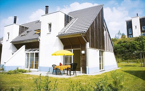 Moderne, witte cottage met een terras en gele parasol in de groene heuvels van Center Parcs Park Hochsauerland.