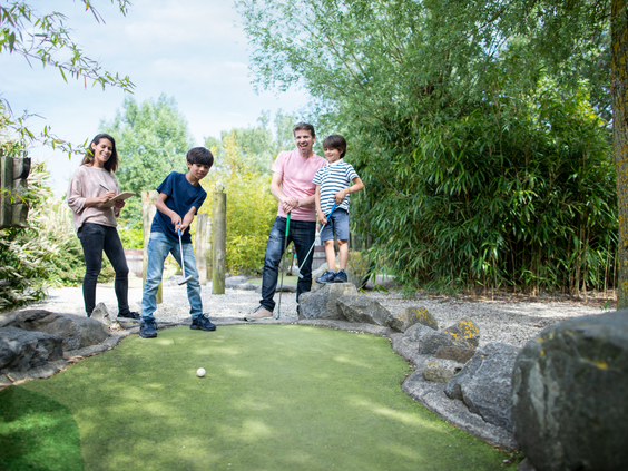 Een gezin met twee zonen speelt een potje midgetgolf op de avontuurlijke golfbaan van Center Parcs Port Zélande in Zuid-Holland.
