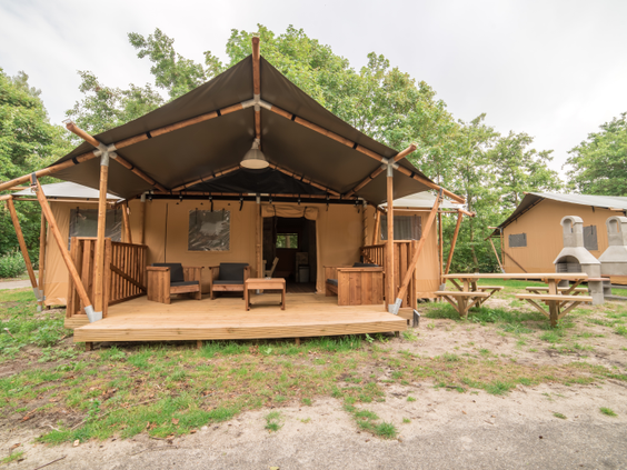 De buitenkant van een luxe safaritent met een ruime houten veranda en een picknicktafel op Center Parcs Port Zélande.