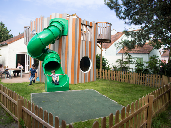 Kinderen spelen in een moderne buitenspeeltuin met een groene glijbaan bij de vakantiehuisjes van Center Parcs Port Zélande.