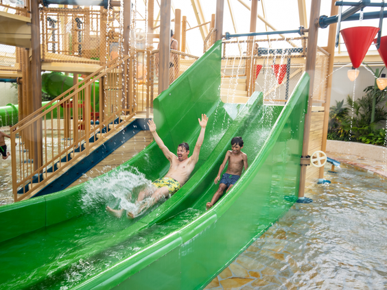 Kinderen glijden samen van de groene glijbaan in het indoor waterparadijs van Center Parcs Port Zélande
