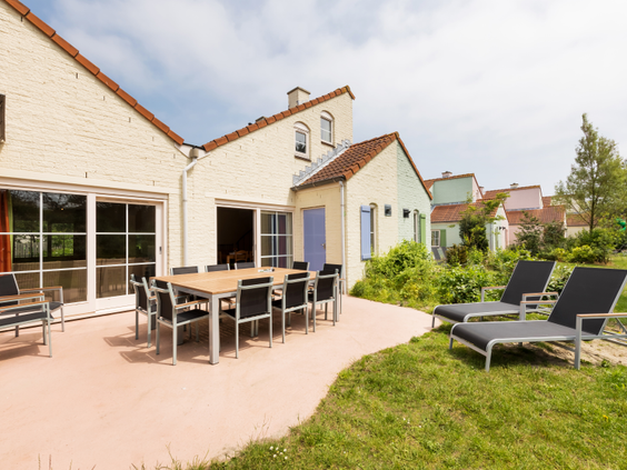 Het ruime terras van een cottage op Center Parcs Port Zélande, met een eettafel en ligstoelen in de tuin.