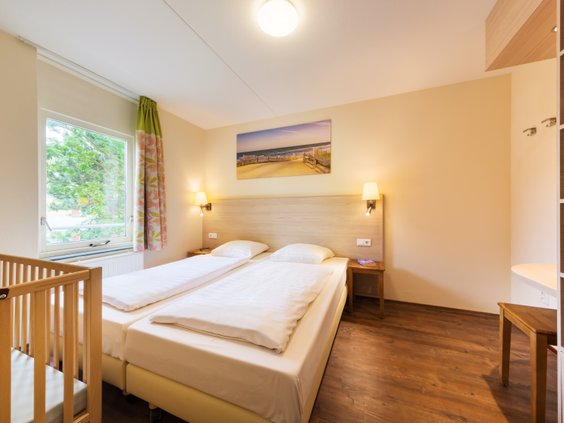 Nette slaapkamer in een hotelkamer of appartement op Center Parcs Port Zélande met een opgemaakt tweepersoonsbed en een kinderbedje.