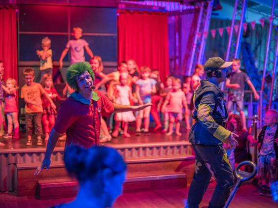 Kinderen dansen en zingen op een podium met het entertainmentteam tijdens een live kindershow op Center Parcs Port Zélande.