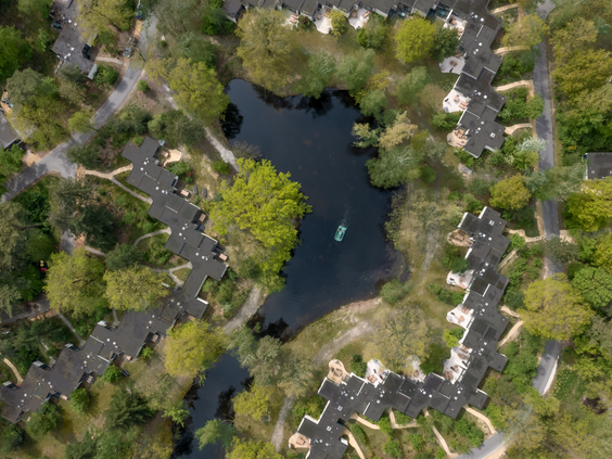 Een luchtfoto van Center Parcs Erperheide, waarop de vele cottages te zien zijn die verspreid liggen tussen de groene bomen en rondom een meer.