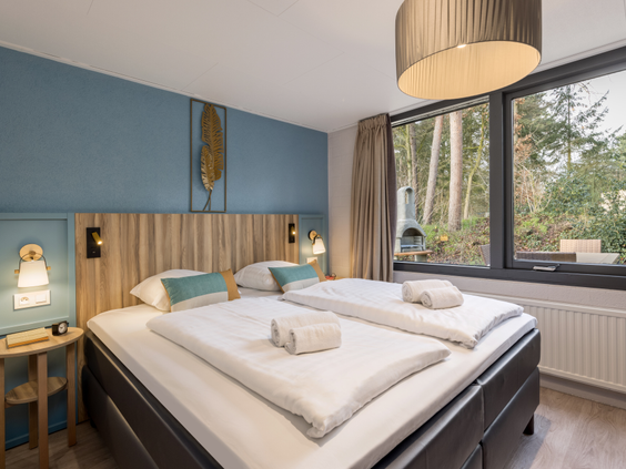 De stijlvolle slaapkamer van een vernieuwde cottage bij Center Parcs Erperheide, met een comfortabel opgemaakt tweepersoonsbed en uitzicht op het bos.