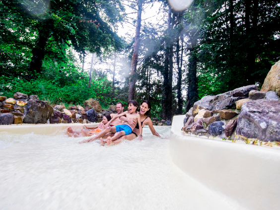 Een gezin glijdt samen door de wildwaterbaan van de Aqua Mundo bij Center Parcs Erperheide, omgeven door groene bomen en rotsen.