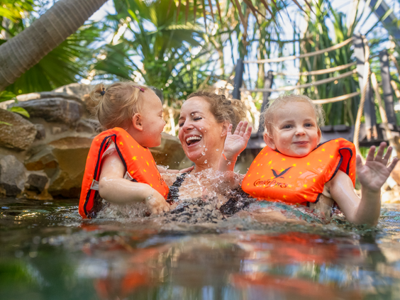 Een lachende moeder heeft plezier met haar twee jonge kinderen, die zwemvestjes dragen, in het water van de Aqua Mundo van Center Parcs Erperheide.