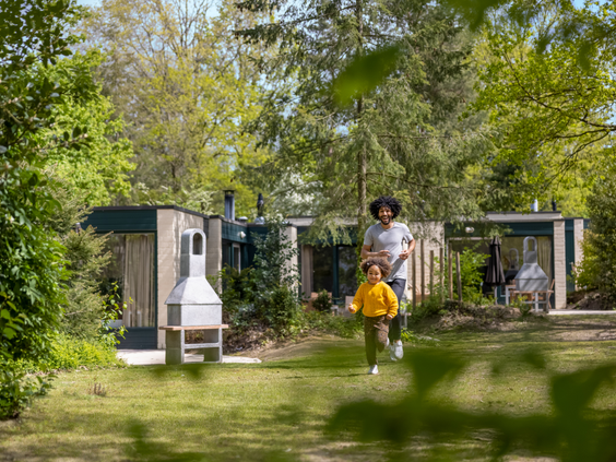 Een kind rent vrolijk door de ruime, groene tuin van een cottage bij Center Parcs Erperheide, met een barbecue op het terras.