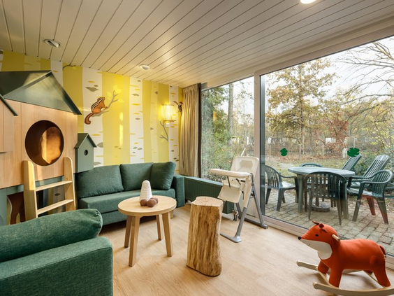 De gezellige woonkamer van een 'Dieren in het bos' themacottage bij Erperheide, met een ingebouwd speelhuisje, een hobbel-vos en uitzicht naar buiten.