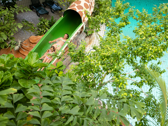 Moeder en dochter glijden van een groene glijbaan met giraffenprint in het tropische zwemparadijs Aqua Mundo van Center Parcs Zandvoort.