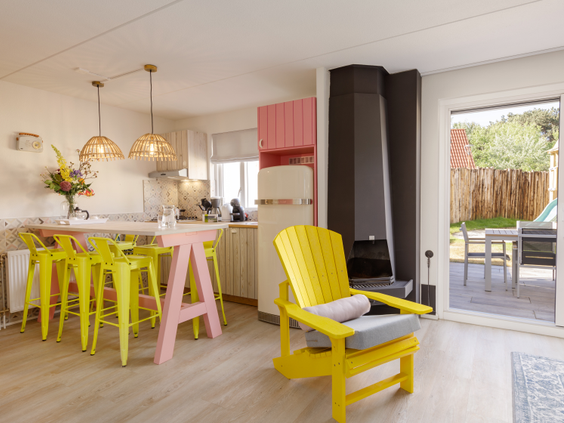 Het kleurrijke en moderne interieur van een vernieuwde cottage bij Center Parcs Zandvoort, met een open keuken en een gele stoel.