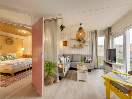 Overzicht van de modern ingerichte woonkamer en een doorkijkje naar de slaapkamer in een cottage van Center Parcs Zandvoort.