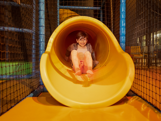 Een lachend meisje komt uit een gele tunnelglijbaan in de softplay indoor speeltuin van Center Parcs Zandvoort.