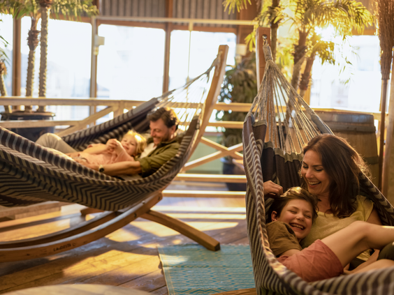 Een gezin ontspant lachend in comfortabele hangmatten in de tropische, overdekte Market Dome van Center Parcs Zandvoort.