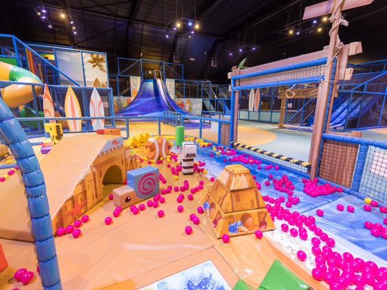 Overzicht van de grote indoor speeltuin de Beach Factory bij Center Parcs Zandvoort, met een grote roze ballenbak en diverse klimtoestellen en glijbanen.