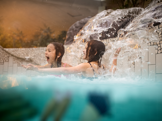 Twee meisjes hebben waterpret en lachen onder een waterval in het zwembad van de Aqua Mundo bij Center Parcs Zandvoort.