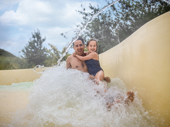Een vader en zijn dochter glijden samen lachend van de brede familieglijbaan in het zwemparadijs van Center Parcs Zandvoort.