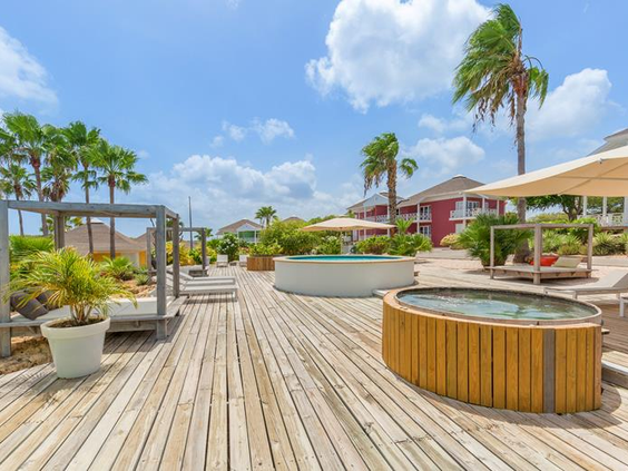 Het ruime houten zonneterras met luxe ronde loungebedden en jacuzzi's bij het zwembad van CHOGOGO Resort op Curaçao.