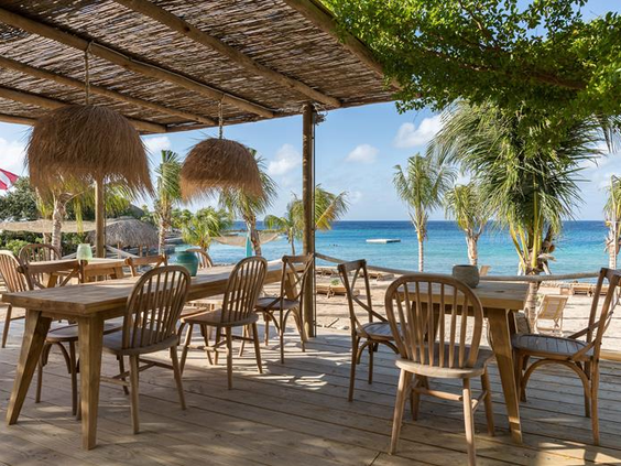 Het sfeervolle houten terras van restaurant KOKO's bij CHOGOGO Resort, met uitzicht op het strand en de blauwe zee.