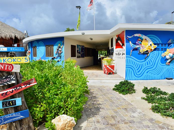 De kleurrijke ingang van duikcentrum Jan Thiel Diving bij CHOGOGO Dive & Beach Resort op Curaçao, met een muurschildering van duikers.