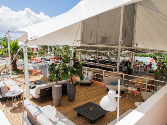 Een trendy loungeterras met witte designmeubels en grote zonnedoeken bij CHOGOGO Resort aan de Jan Thiel baai.