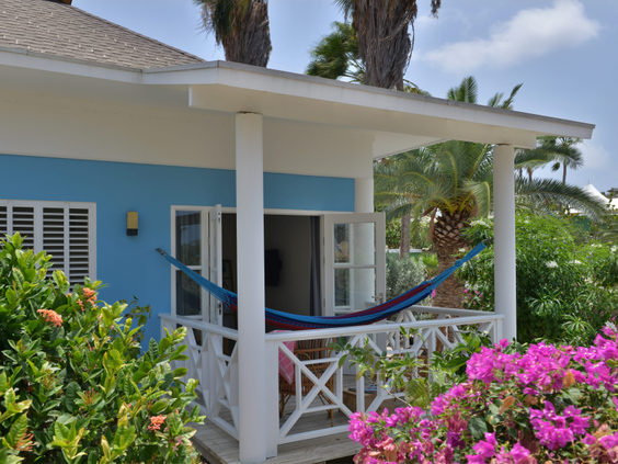 Een blauw geschilderde bungalow bij CHOGOGO Resort met een veranda en hangmat, omgeven door tropische bloemen.