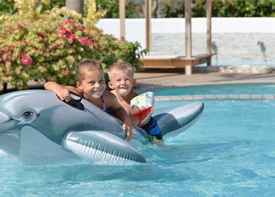 Twee lachende kinderen die spelen op een grote opblaasbare dolfijn in het zwembad van CHOGOGO Resort.