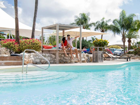 Een gezin dat ontspant op een comfortabel loungebed onder een overkapping bij het zwembad van CHOGOGO Dive & Beach Resort.