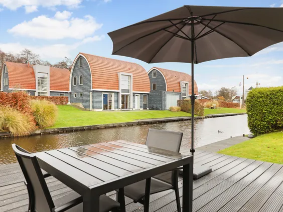 Een groot vlonderterras met een tuinset en parasol, direct aan het water bij een vakantiewoning op Villapark de Bloemert.