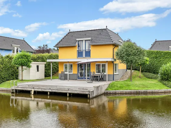 Een gele watervilla met een zeer groot houten vlonderterras boven het water, ideaal om aan te leggen met een bootje.