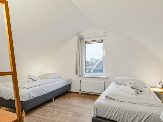 Nette slaapkamer met twee eenpersoonsbedden onder een schuin dak in een vakantiehuis op Villapark de Bloemert.