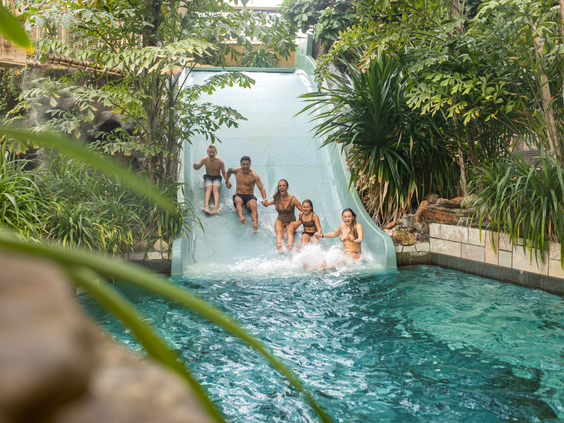 Een gezin van vijf personen glijdt tegelijkertijd lachend naar beneden van de extra brede familieglijbaan in het tropische zwemparadijs Aqua Mundo van De Eemhof.