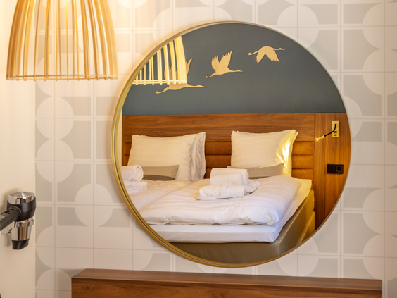 De reflectie van een comfortabel opgemaakt bed in een ronde spiegel in de sfeervolle slaapkamer van een hotelappartement bij Center Parcs De Eemhof.