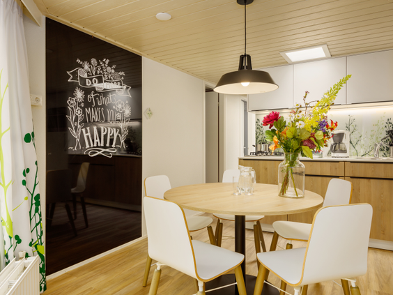 De stijlvolle eethoek met een ronde tafel en witte stoelen in een vernieuwde cottage van Center Parcs De Eemhof, met een groot schoolbord aan de muur.