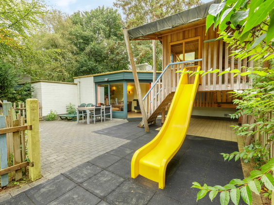 Een Nieuwe Generatie Kindercottage bij De Eemhof met een eigen omheinde achtertuin met een houten speelhuisje en een gele glijbaan.
