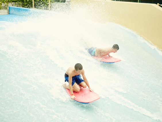 Twee jongens leren surfen op de Flow Rider surfsimulator in de Aqua Mundo van Center Parcs De Eemhof, liggend op hun bodyboards op de golf.