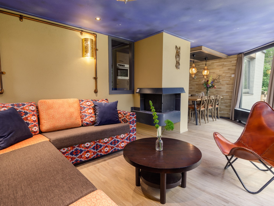 De sfeervol ingerichte woonkamer van een Avontuur cottage bij De Eemhof, met een kleurrijke hoekbank, een open haard en een opvallend blauw plafond.
