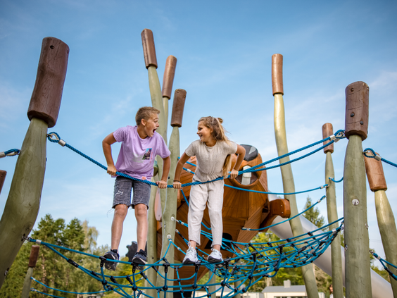 Een jongen en een meisje klimmen en spelen samen in een groot touwenparcours in een van de buitenspeeltuinen van Center Parcs De Eemhof.