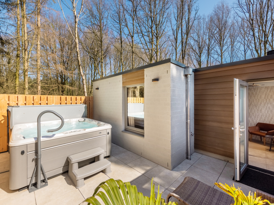Het luxe privéterras van een wellness-cottage bij De Eemhof, uitgerust met een ruime jacuzzi en een buitensauna, omringd door bomen.