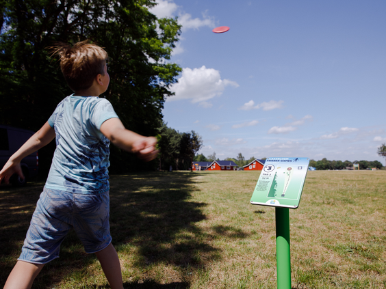 Een kind gooit een frisbee op het grote speelveld van Molecaten Park De Flaasbloem tijdens een potje discgolf.