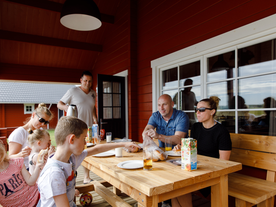 Een familie ontbijt samen aan een picknicktafel op de veranda van hun rode vakantiehuis op Molecaten Park De Flaasbloem.