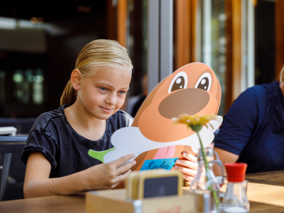 Een meisje knutselt een papieren figuur van de Molecaten-mascotte aan een tafel in het restaurant van De Flaasbloem.