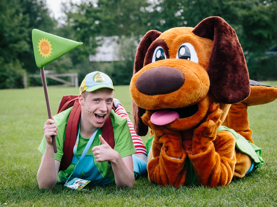 De Molecaten-mascotte en een animatiemedewerker liggen vrolijk in het gras op Molecaten Park De Flaasbloem, klaar voor avontuur.