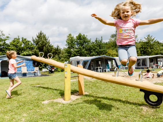 Twee meisjes spelen op een houten wipwap in de speeltuin, gelegen op een kampeerveld van Molecaten Park De Flaasbloem.