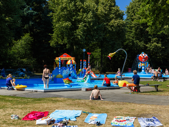 Kinderen spetteren en spelen in het vrolijk gekleurde spraypark van Molecaten Park De Flaasbloem, een buitenzwembad met kinderglijbanen en waterspuiters.