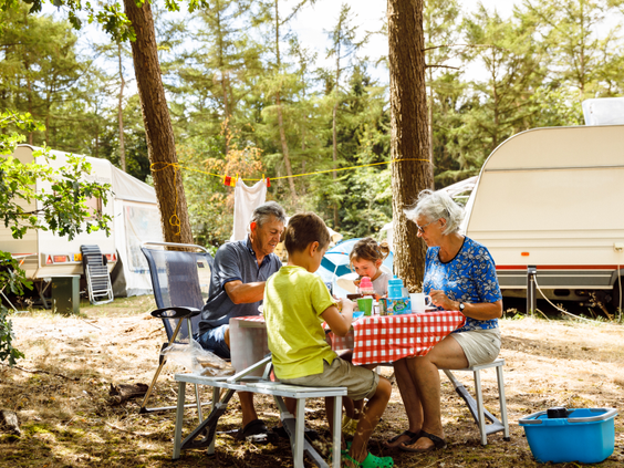 Grootouders met hun kleinkinderen genieten van de vakantie op een kampeerplaats met caravan op Molecaten Park De Flaasbloem.