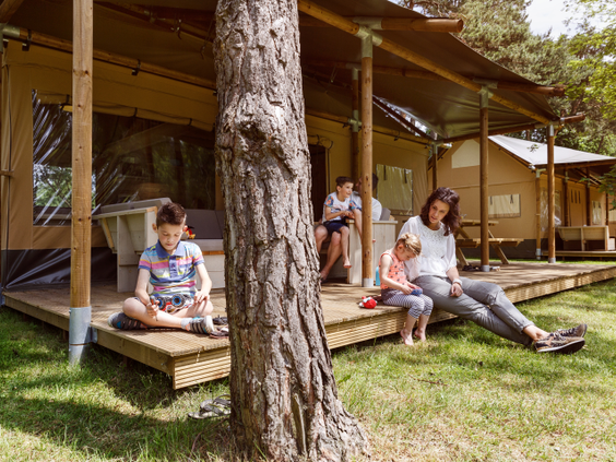 Een gezin ontspant op de houten veranda van een luxe safaritent op Molecaten Park De Flaasbloem, een glamping-accommodatie.